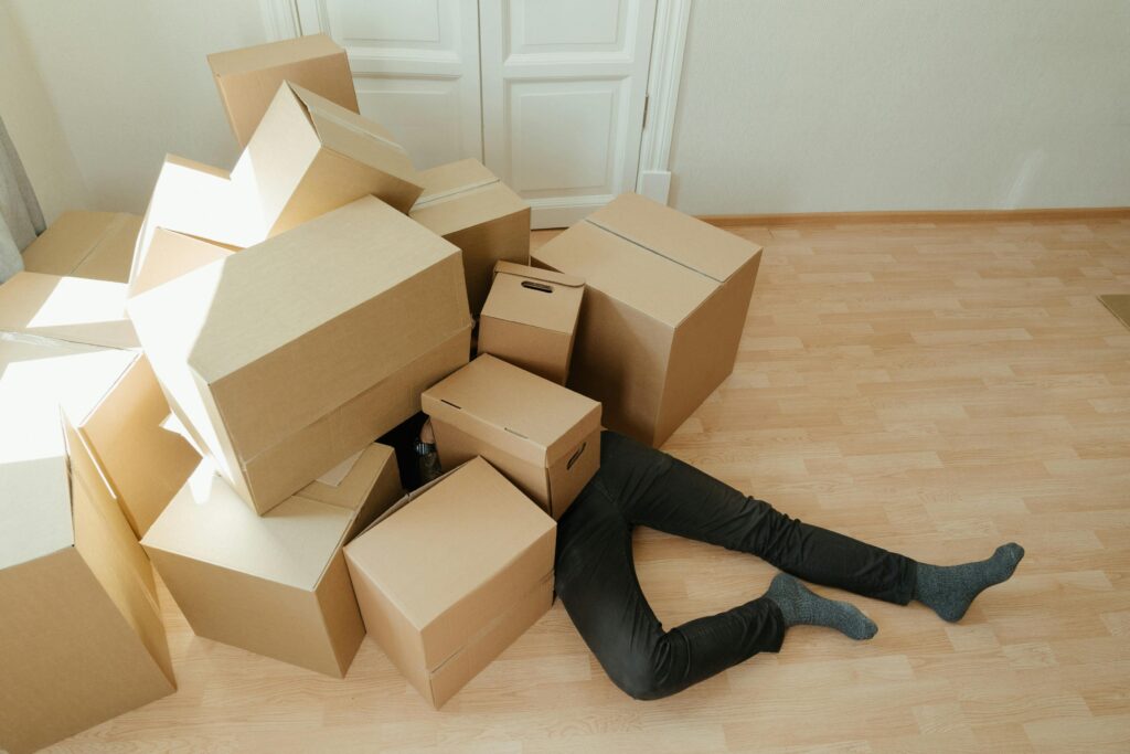 pexels-photo-4553182-4553182 A person overwhelmed by cardboard boxes during a home move, symbolizing stress and relocation.